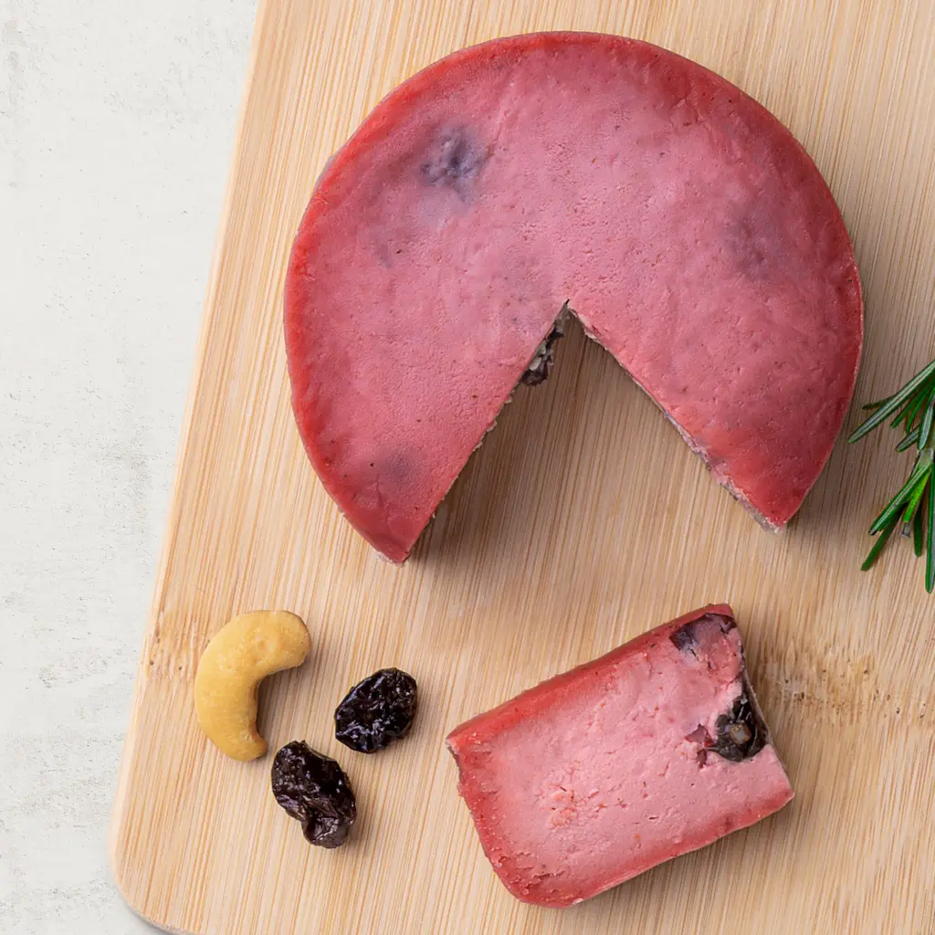 Queijo de Castanha de Caju com Cranberry em uma tábua de madeira, vista de cima. O queijo tem uma linda cor rosa.