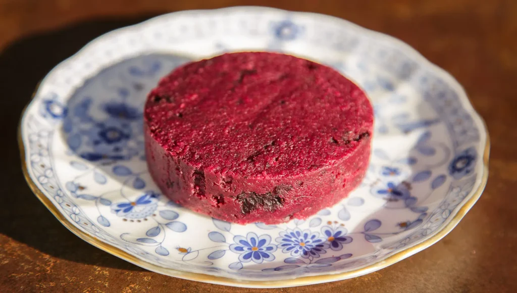 Queijo de Castanha de Caju com Cranberry de cor rosa típica em um prato branco com florzinhas azuis.