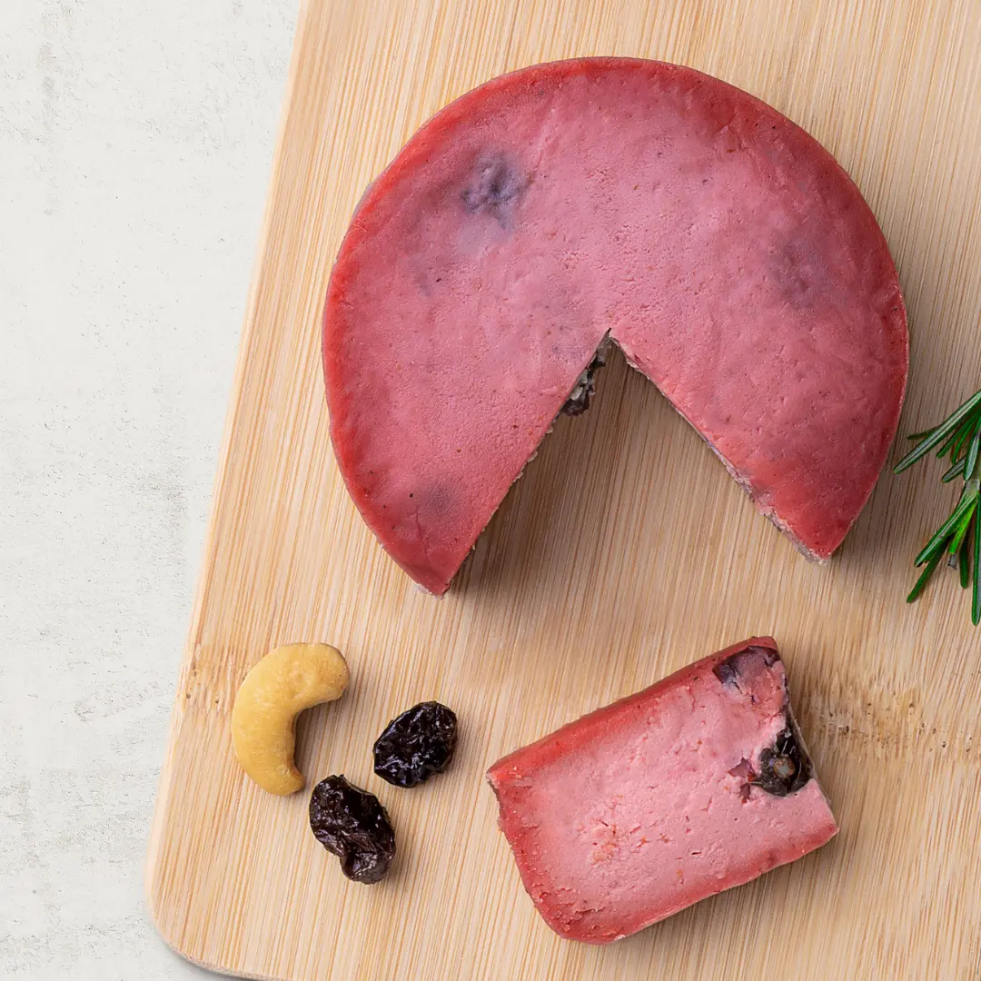 Queijo de Castanha de Caju com Cranberry sobre uma tábua de madeira, visto de cima. O queijo tem cor rosa.