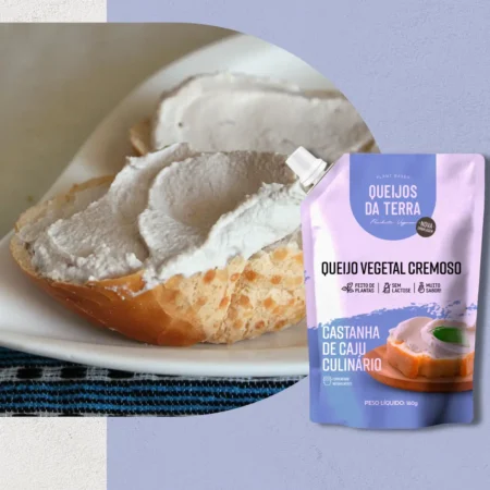 Queijo Cremoso de Castanha de Caju Culinário. Em primeiro plano, a embalagem azul-clara vista de frente. Ao fundo, o queijo cremoso espalhado sobre um pedaço de pão.