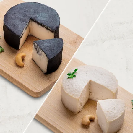 O kit contém 2 Queijos de Castanha de Caju: 1 Queijo de Castanha de Caju Defumado e 1 Queijo de Castanha de Caju com Gergelim. Os queijos são fotografados de lado.