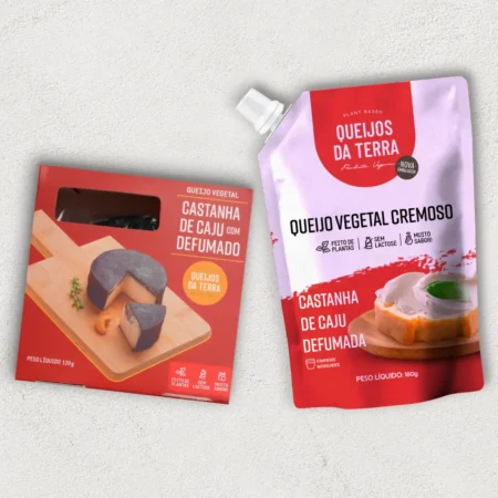 O kit contém 2 Queijos de Castanha de Caju: 1 Queijo de Castanha de Caju Defumado e 1 Queijo de Castanha de Caju Cremoso Defumado, em embalagem tipo pouch. Ambos vêm em embalagens vermelhas.