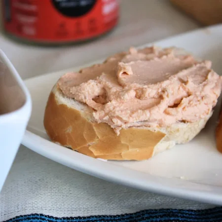 Queijo Cremoso de Castanha de Caju com Tomate Seco e Orégano, de cor laranja-clara, espalhado sobre um pedaço de pão.